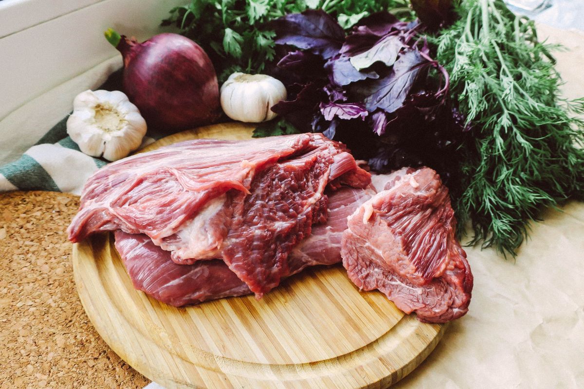 Rohes Fleisch mit frischen Kräutern und Gemüse auf einem Holzbrett