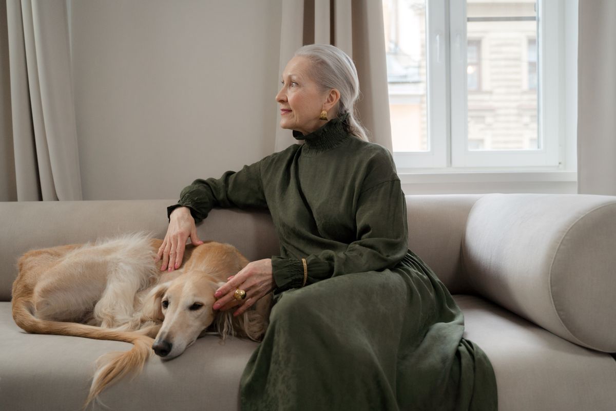 Ältere Frau sitzt ruhig auf dem Sofa, ihr Hund hat den Kopf entspannt an sie gelehnt